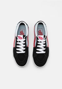 Sorte semskete sneakers med røde stripes på siden og hvite snøringer. Har polstret tunge og krage, hvit mellomsåle og gummisåle.
