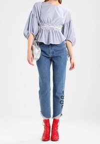 Randig blå och vit blus med puffärmar, åtdragen i midjan. Blå jeans med grön broderad detalj på benet. Röda ankel stövlar.