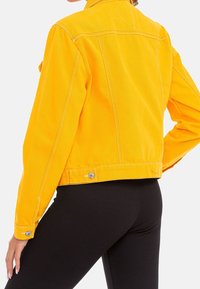 Yellow denim jacket with a cropped design, stitched detailing, and silver hardware accents. Features a classic collar and buttoned cuffs.