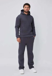 Hoodie gris foncé et pantalon de survêtement assorti en tissu doux, avec une poche avant, une capuche attachée et des poignets côtelés. Baskets blanches.