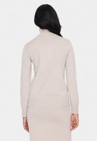 Beige tajt turtlenecktröja med ribbad mudd och nederkant. Mjuk textur, rena linjer och sömlös design, lämplig för lager-på-lager.