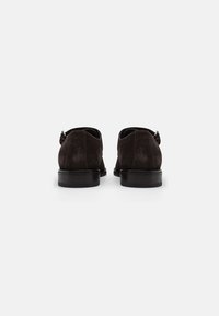 Chaussures en suede brun foncé avec une texture lisse, de forme ronde et un petit talon. Présentent un design subtil sans lacets et un minimum de détails matériels.