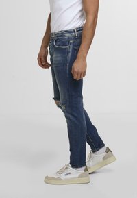 Blugi skinny de culoare albastru închis, cu detalii uzate și o croială ajustată. Asortați cu adidași albi și gri deschis. Tricou alb simplu.