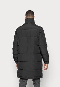 Giacca imbottita nera con collo alto, caratterizzata da sezioni trapuntate orizzontali e polsini elasticizzati, progettata per garantire calore e protezione.