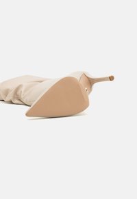 Botte à talons aigus beige avec un bout pointu et une texture lisse. La semelle est marron clair avec un motif strié pour éviter le glissement.