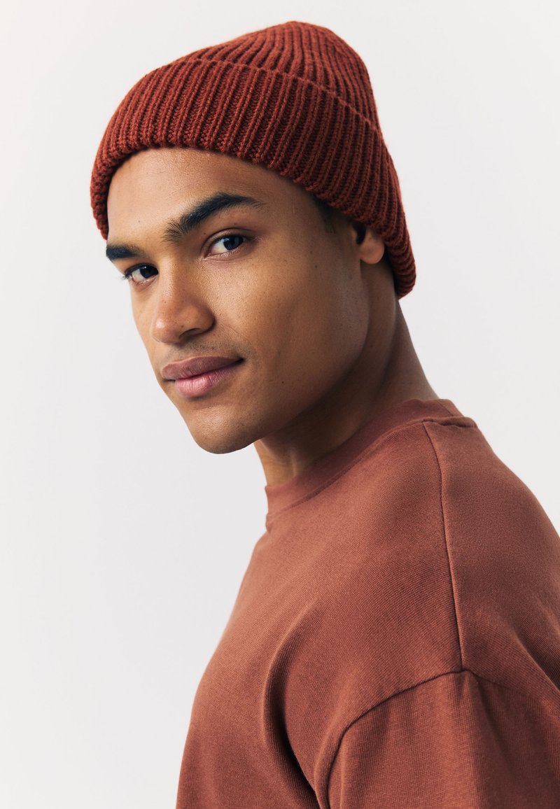 Kapa boje hrđe, pletena s rebrastom teksturom, uparena s odgovarajućom jednobojnom majicom boje hrđe s okruglim izrezom i kratkim rukavima.