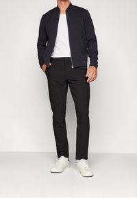 Marineblå bomberjakke med lynlås over en hvid t-shirt, parret med sorte bukser og hvide sneakers. Jakken har en glat tekstur og ribbede manchetter.