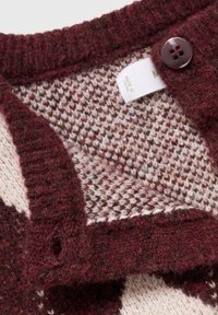 Vinsko rdeča pletena kardigan s houndstooth vzorcem. Ima zapiranje na gumbe, mehak občutek in oznako za nego vidno znotraj.