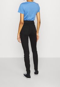 Blue short-sleeve t-shirt paired with high-waisted black skinny jeans and black sneakers. The outfit is fitted and casual.
