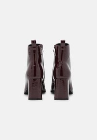 Bordowe lakierowane botki za kostkę z kwadratowym noskiem i grubym obcasem, wyposażone w zamek błyskawiczny i sięgające do kostki. Błyszczące wykończenie o gładkiej fakturze.