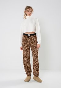 Skraćeni bijeli pleteni turtleneck, uparen s labavim hlačama na jogger leopard uzorka u nijansama narančaste i crne, s elastikom u struku.
