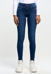 Jeans ajustados de mezclilla en color azul, con una cintura media, corte slim y detalles de costura sutiles. Combinados con zapatillas blancas.