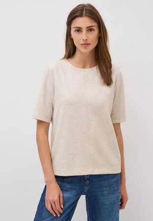 Beige Kurzarmoberteil aus weichem, strukturiertem Stoff, mit runder Ausschnitt und geradem Schnitt. Getragen mit blauen Jeans.