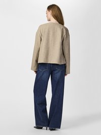 Jachetă scurtă dintr-un amestec de lână bej, cu o croială dreaptă, asortată cu blugi din denim de un albastru închis, cu talie înaltă și picioare largi. Textură netedă și detalii minime.