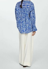 Blue floral-patterned long-sleeve shirt with gathered back detail, paired with cream wide-leg trousers. Soft fabric texture and loose fit.