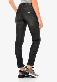 Jeans skinny noirs avec une décoloration subtile, un design à cinq poches et un motif de couture sur la taille. Associés à des baskets métalliques à lacets.