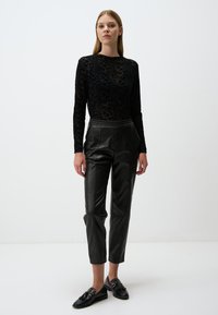 Schwarzes, durchsichtiges Langarmoberteil mit floralem Muster, kombiniert mit hoch taillierten, schwarzen Kunstlederhosen und schwarzen Loafers.