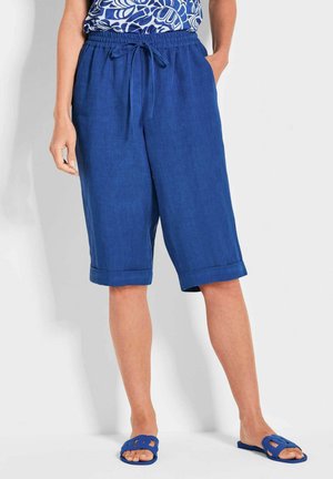 Blauwe linnen shorts met een elastische tailleband en een trekkoord, voorzien van omgeslagen zoom en zakken. Gecombineerd met blauwe sandalen.