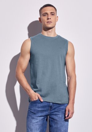 Camiseta sin mangas de algodón azul con escote redondo, que presenta un logo sutil en el pecho y un corte holgado, combinada con jeans de mezclilla.