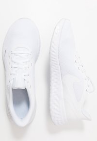 Zapatillas deportivas blancas con parte superior de malla, punta redondeada, suela de goma texturizada y diseño clásico de cordones. Marca sutil en los laterales.