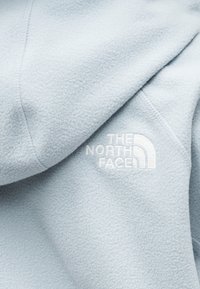 Φωτεινό γαλάζιο φλις φούτερ με διακ ριτική υφή, με λευκό κεντημένο λογότυπο στο μπροστινό μέρος. Απλός, μοντέρνος σχεδιασμός με κουκούλα.