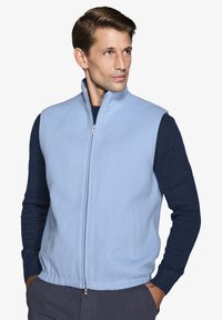 Gilet in pile azzurro chiaro con colletto alto, zip frontale e tasche laterali, abbinato a una camicia a maniche lunghe textured blu scuro.
