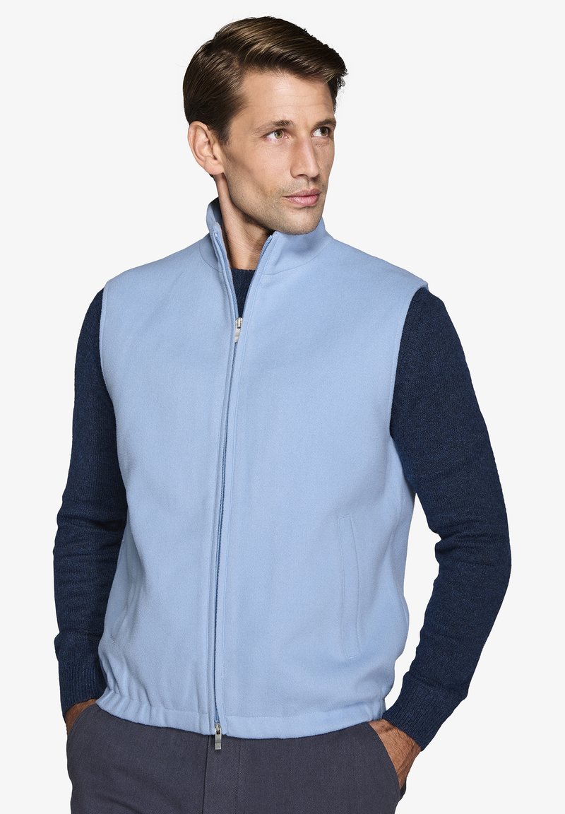 Gilet in pile azzurro chiaro con colletto alto, zip frontale e tasche laterali, abbinato a una camicia a maniche lunghe textured blu scuro.