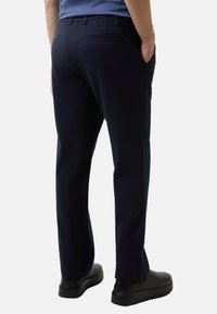 Marineblauwe sweatpants met een relaxte pasvorm, voorzien van twee achterzakken en zijnaad, gecombineerd met zwarte schoenen. Zachte textuur en eenvoudig ontwerp.