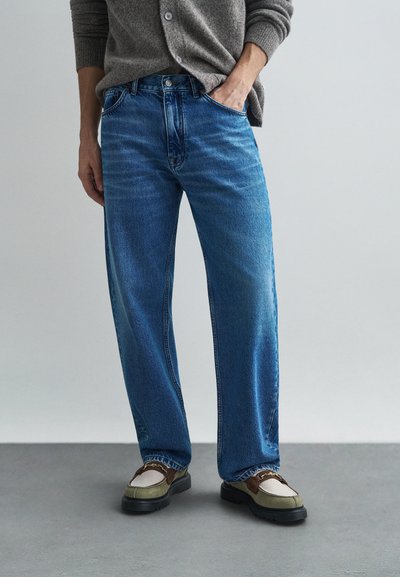 Jean en denim bleu clair, avec une coupe ample, un design à cinq poches et une finition délavée. Associé à des chaussures épaisses à plusieurs teintes. Cardigan gris texturé.