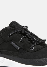 Black sneaker with a textured fabric upper, elastic laces, cinch closure, and white rubber sole. Timberland logo is visible on the side.