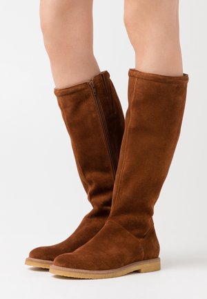 Botas altas de ante marrón con un diseño estilizado y un detalle de cremallera lateral, con suela plana y textura suave.