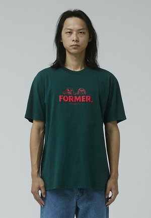 Green oversized T-shirt featuring a red graphic with the word "FORMER." and cartoon faces. Made of cotton with short sleeves and a crew neck.