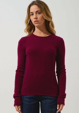 Pull-over en tricot bordeaux à manches longues, avec un col rond et des poignets côtelés, fabriqué en tissu doux et texturé.