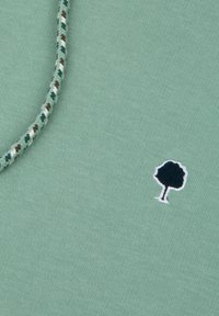 Green cotton fabric featuring a textured, woven rope detail and a small embroidered tree logo in dark blue and white.