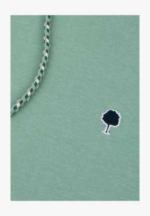 Groene katoenstof met een textuur, geweven touwdetail en een klein geborduurd boompje logo in donkerblauw en wit.