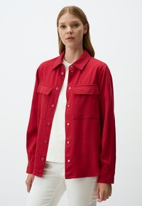 Chemise rouge à boutons en tissu lisse, dotée de deux poches sur la poitrine, d'un col pointu et de longues manches avec des poignets boutonnés.