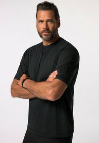Sort kortærmet t-shirt lavet af bomuld, med et mærke på venstre ærme og en rund halsudskæring med synlige sømdetaljer.