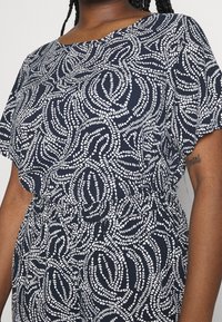 Marinblå klänning med vitt abstrakt virvelmönster, lös passform med korta ärmar och elastisk midja. Slät tygtextur, avslappnad design.