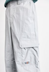 Pantalon cargo gris clair en tissu texturé avec une taille élastique, des poches latérales et un patch logo sur la cuisse.