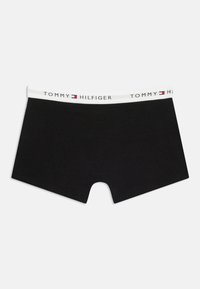 Μαύρα ανδρικά μποξεράκια με λευκή ελαστική ζώνη στη μέση που φέρει το κείμενο "Tommy Hilfiger" και το λογότυπο της μάρκας σε κόκκινο, λευκό και μπλε.