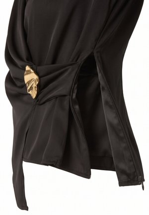 Prenda de satén negro con apertura lateral de cremallera y cierre decorativo dorado con forma de hoja sobre tela fruncida.