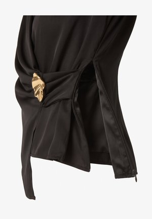 Vêtement en satin noir avec une ouverture latérale à fermeture éclair et une boucle décorative dorée en forme de feuille sur un tissu froncé.