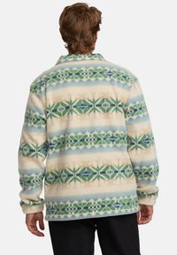 Fleece košile s vícebarevným geometrickým vzorem, která má zelené a modré akcenty na krémovém pozadí. Volný střih, dlouhé rukávy, límec.