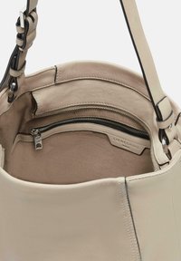 Wnętrze torebki z jasnobeżowej skóry z kieszenią na zamek. Miękka tekstura, minimalistyczny design i widoczny detal logo na podszewce.