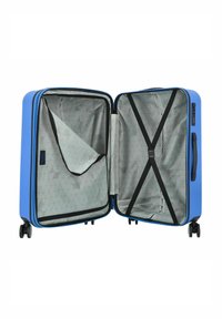 Maleta dura azul con un interior de patrón geométrico gris, correas interiores y un bolsillo con cremallera lateral. Cuenta con cuatro ruedas y un asa lateral.