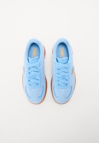 Light blue suede sneakers with rounded toe, flat laces, and tan rubber sole. Features a small branded tag on the side.