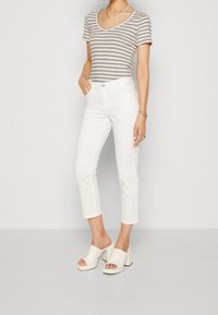 White cropped pants paired with a gray and beige striped t-shirt. Model wears beige heeled mules. Simple design, soft texture, and fitted shape.