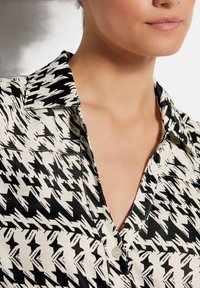 Schwarz-weißer Hahnentrittmuster-Hemd mit Kragen, Knopfverschluss und glatter Stoffoberfläche; hat einen tiefen V-Ausschnitt.