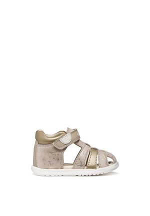 Toddler's beige and gold closed-toe sandal with adjustable Velcro strap and floral pattern, featuring a white flexible sole.