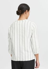 Witte blouse met verticale zwarte strepen, driekwart mouwen en een gestructureerde stof. Kenmerkt zich door een ronde halslijn en een losse pasvorm.